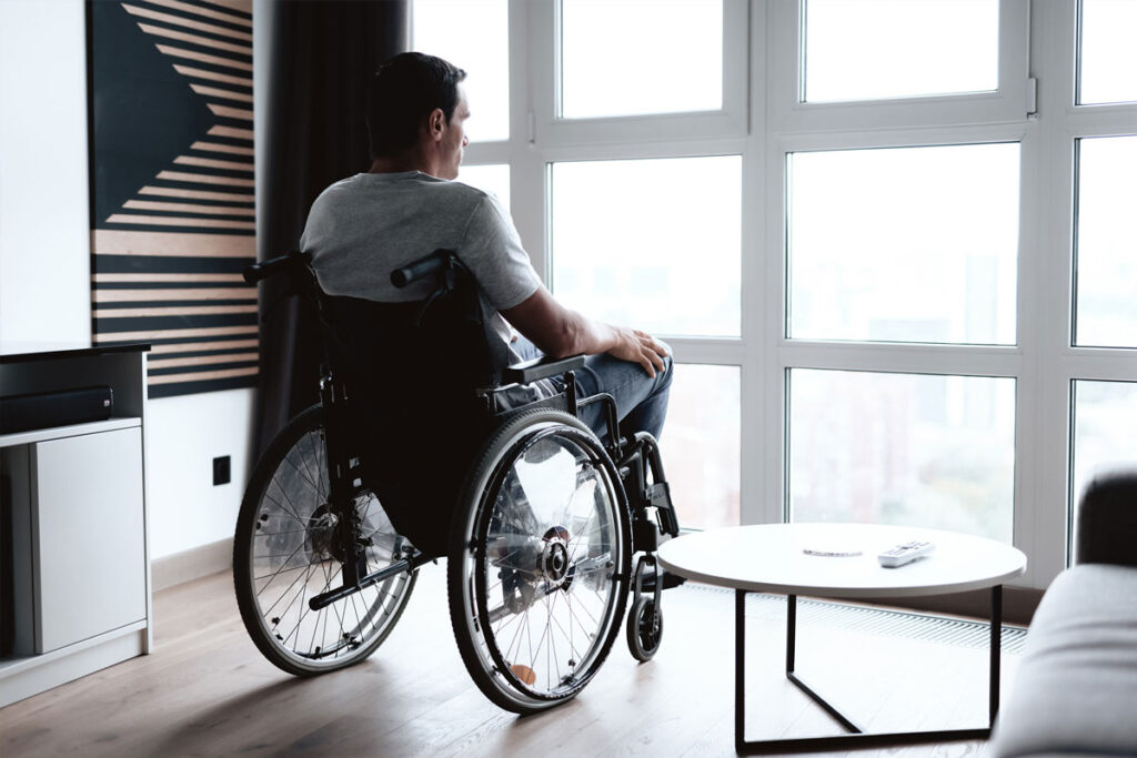 Man in wheelchair looks out the window of his apartment